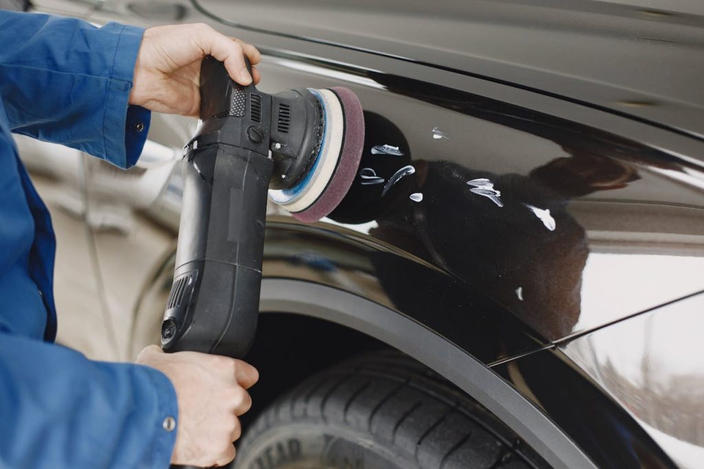 Hands using a polishing machine on a cars surface in a garage setting.